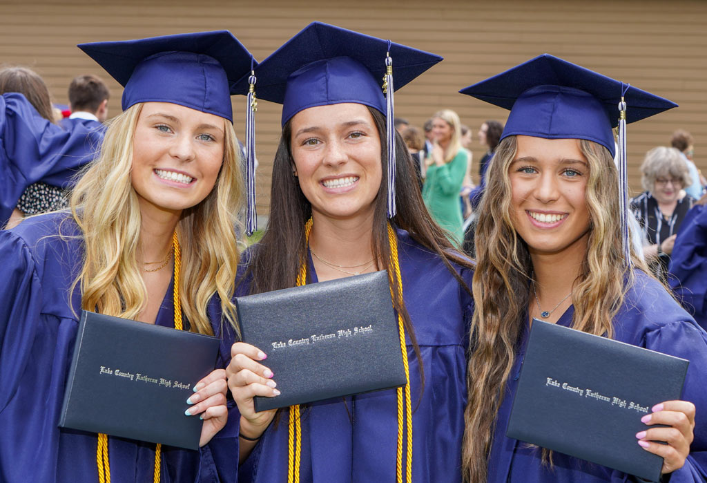 three graduates holding diplomas